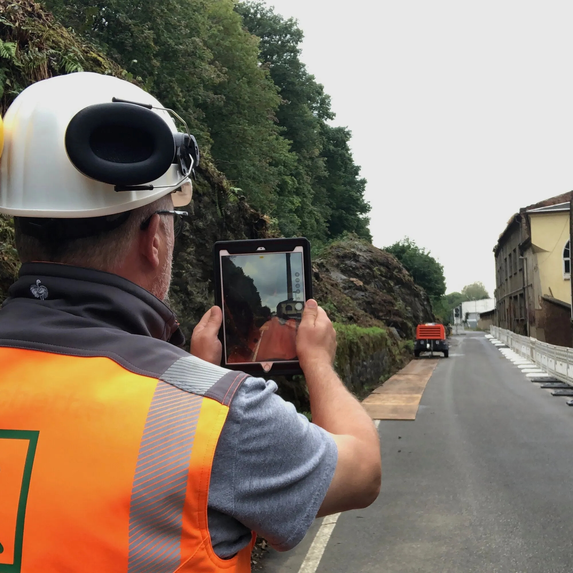 Koordinator mit Helm und Gehörschutz fotografiert eine Baustelle mit dem Tablet